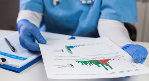 Closeup of person wearing doctor's scrubs and stethoscope, looking at printed report with charts